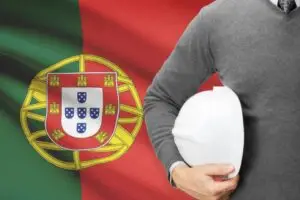 Bandeira de Portugal ao fundo com trabalhador segurando um capacete de segurança, representando o visto de trabalho em Portugal para estrangeiros.