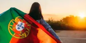 Mulher segurando uma bandeira de Portugal ao pôr do sol, simbolizando a conquista da nacionalidade portuguesa por tempo de residência.