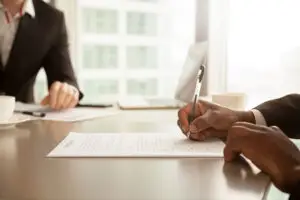 Pessoa assinando um documento de contrato em uma reunião, representando o direito à herança em Portugal para estrangeiros e residentes não habituais.