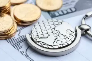 Moedas, notas de dólar e um globo terrestre em miniatura, ilustrando a tributação internacional e a bitributação entre Brasil e Portugal.