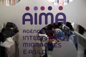 Logotipo da AIMA (Agência para a Integração, Migrações e Asilo) em um balcão de atendimento, relacionado aos primeiros agendamentos de reagrupamento familiar em Lisboa.